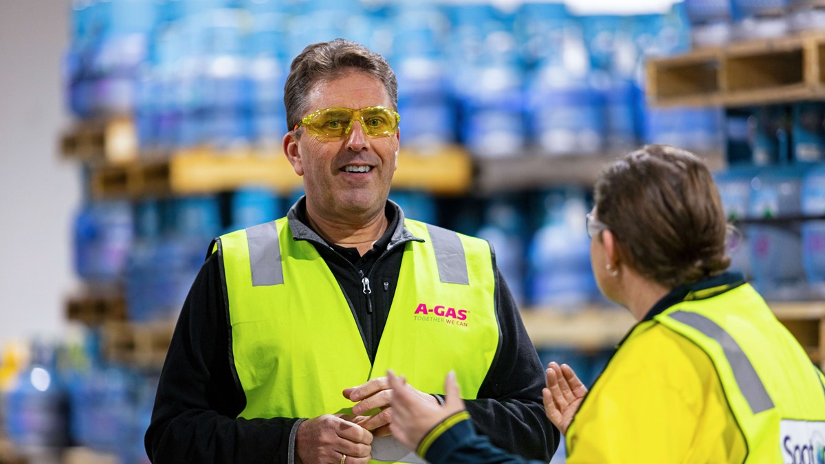 A man smiling and looking at the camera while talking to a female colleague