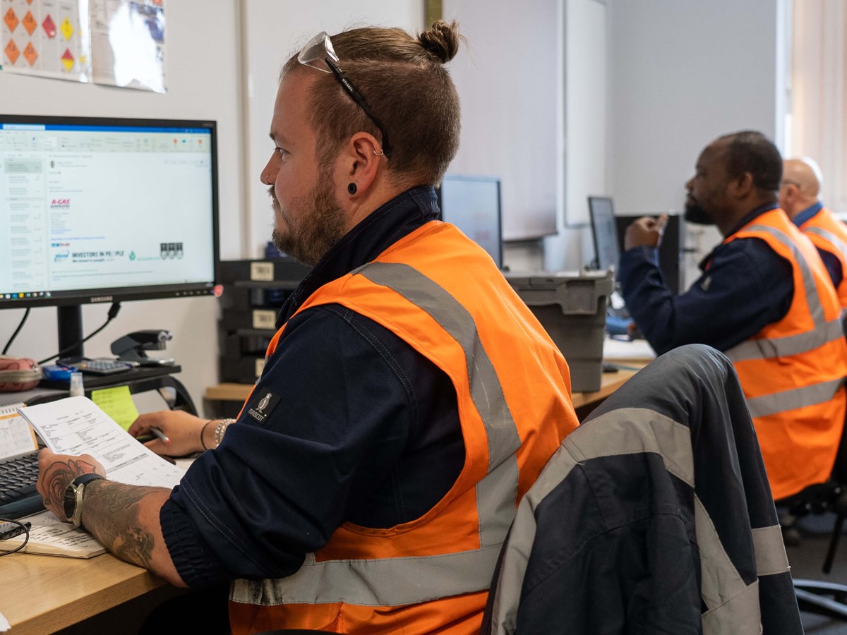 Man in high-vis jacket holds paper while working at a computer