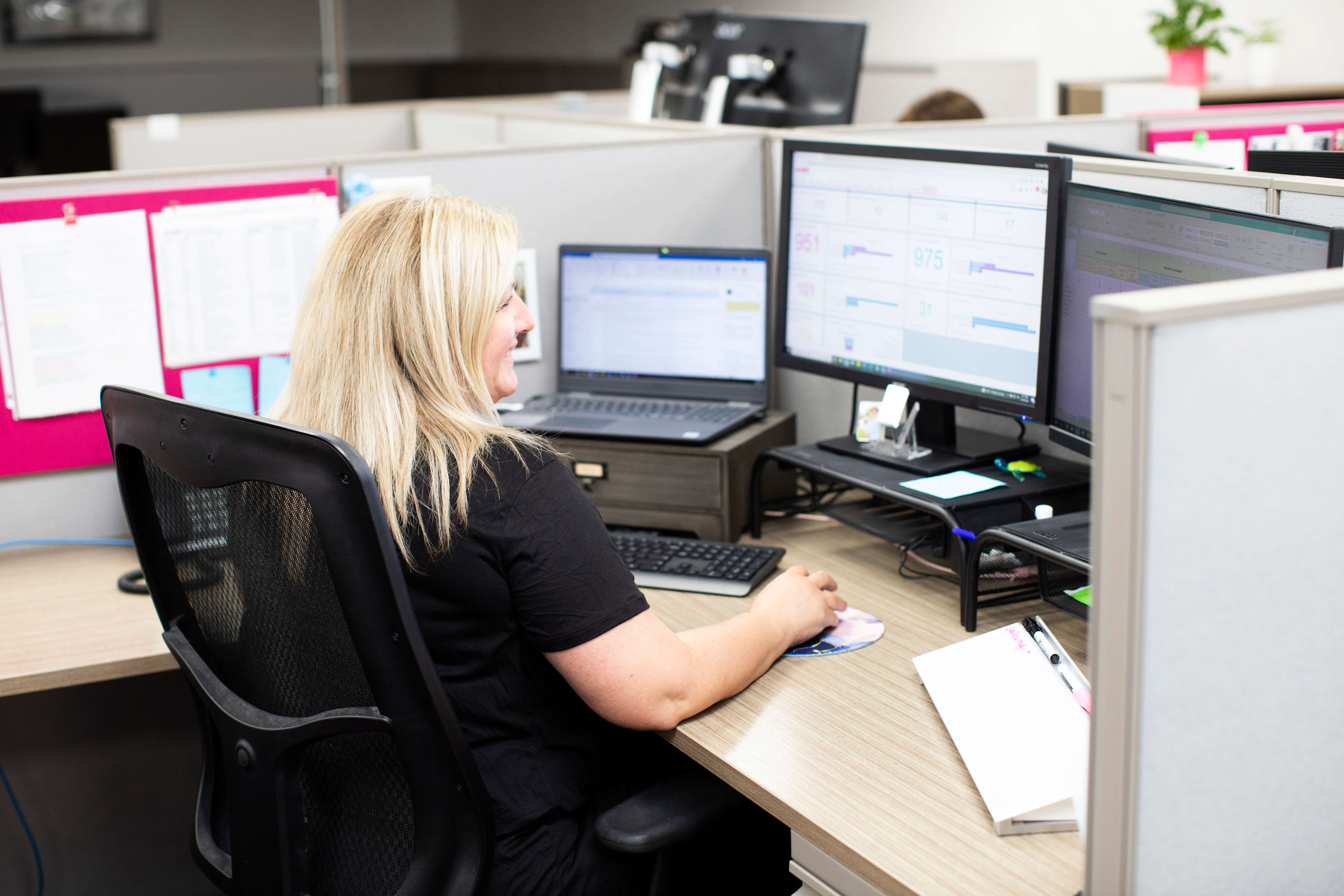 A photo taken from behind of a person sitting in an office pod using their laptop and computer