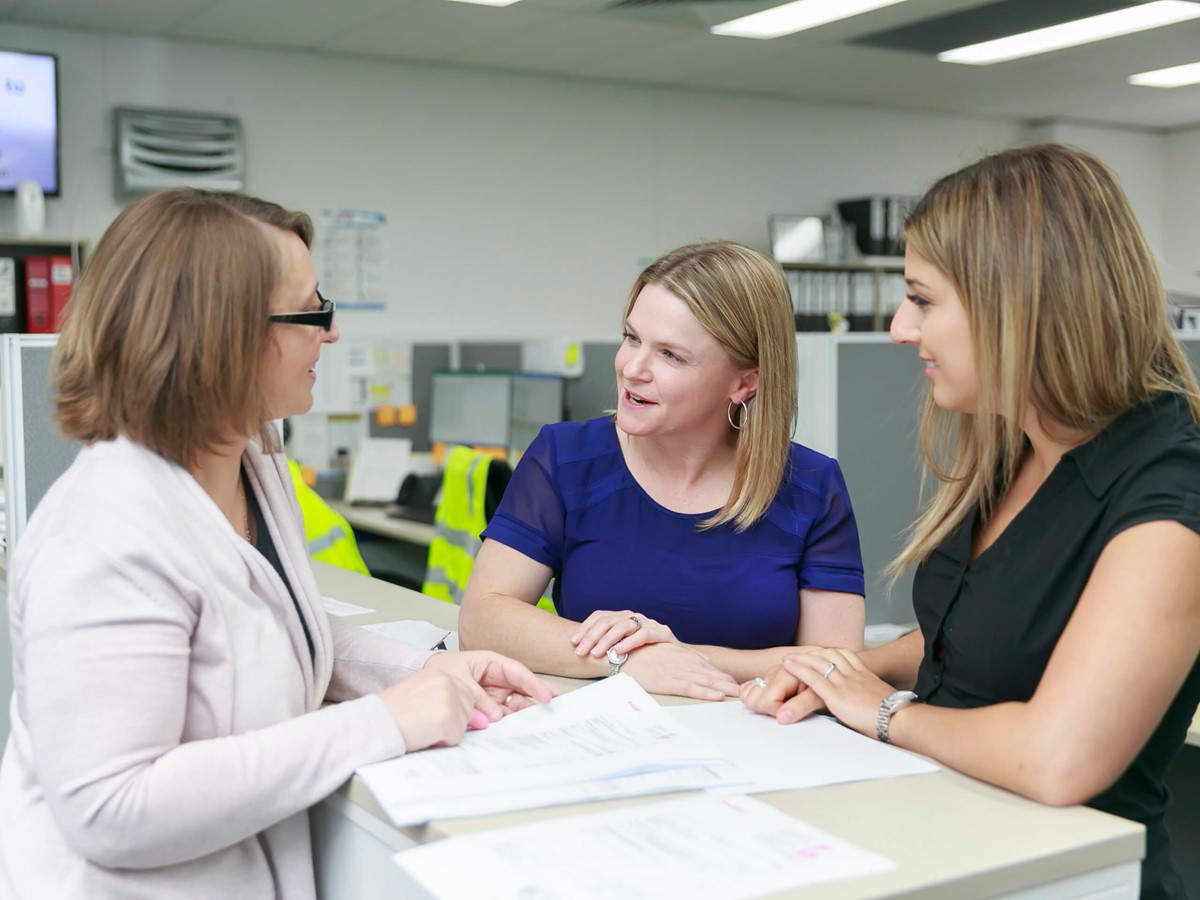 Three women stood talking to each other, they are smiling