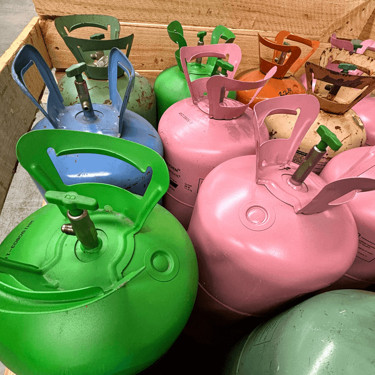 Green, blue and pink cylinders in a wooden crate in a warehouse