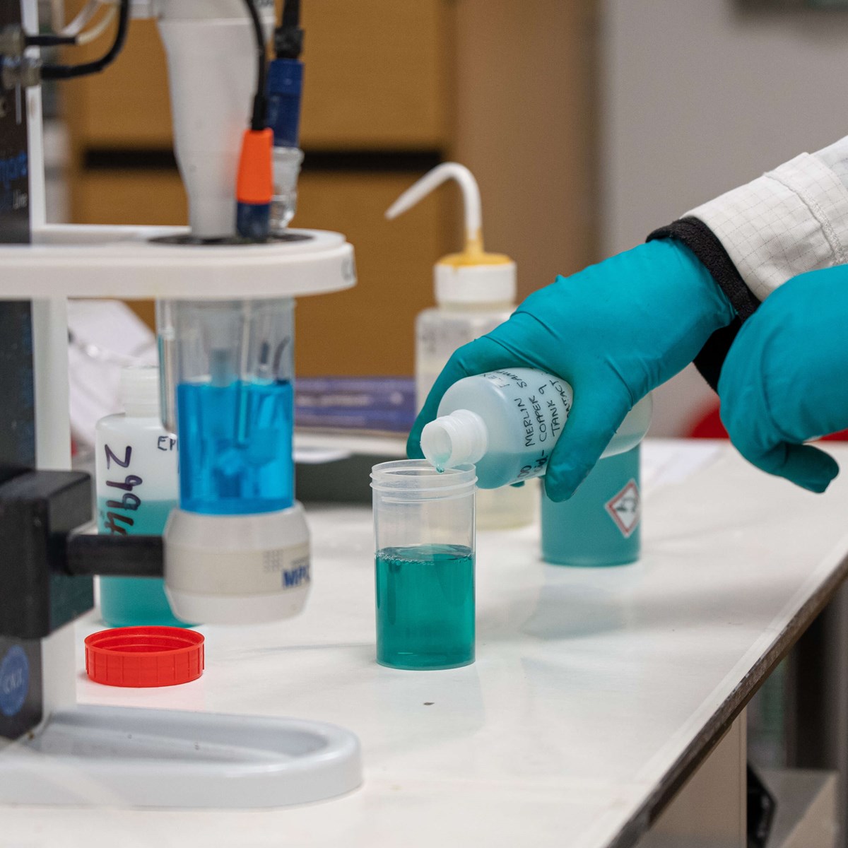 Man pours green liquid into plastic container from the side in laboratory