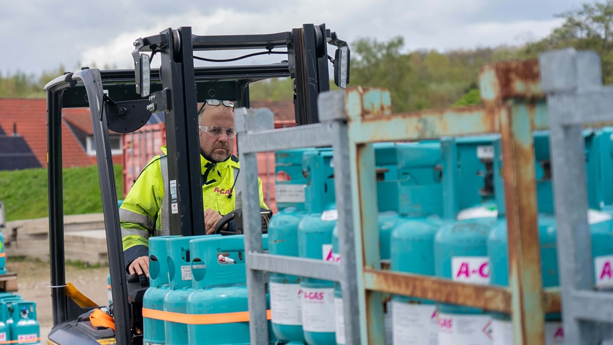 A man in a high-vis yellow jacket moving blue cylinders with a forklift truck