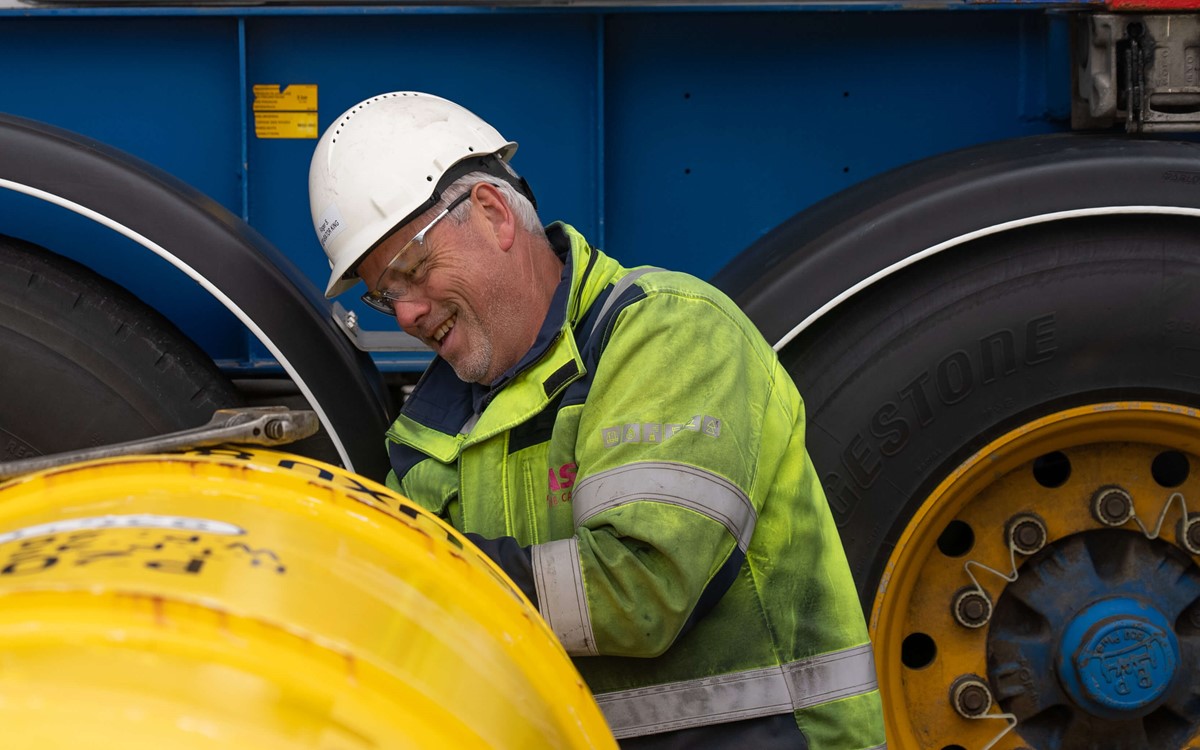 Man in a helmet and yellow hi-vis jacket laughing while working on a yellow tank