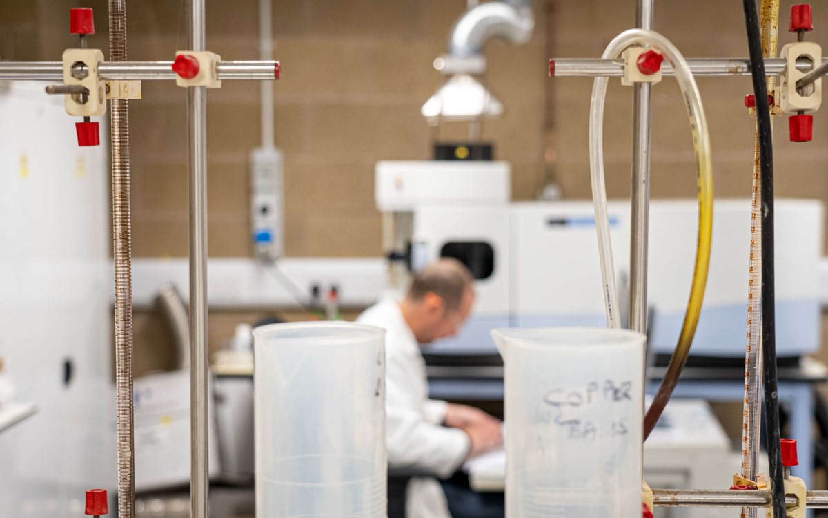Two plastic jugs and scientific equipment with man in the background