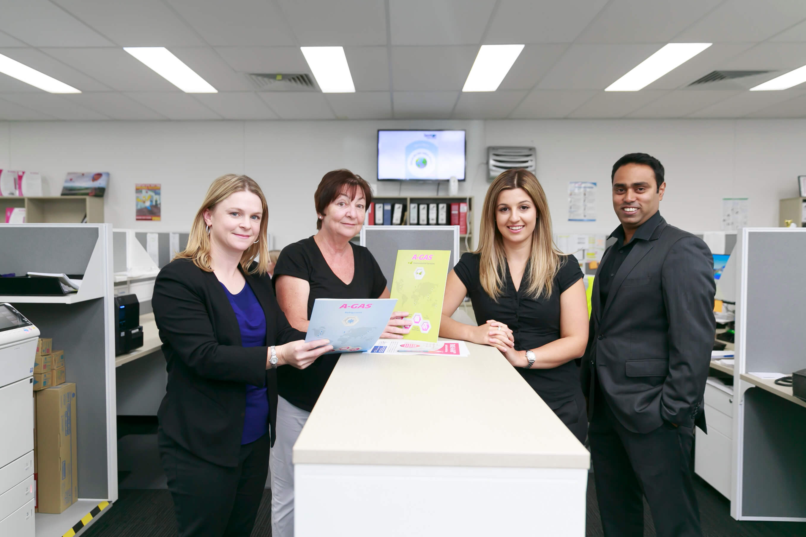 four workers in office environment looking at camera and smiling