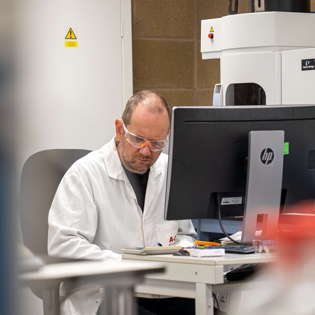 Man in white coat sits at a computer in in laboratory