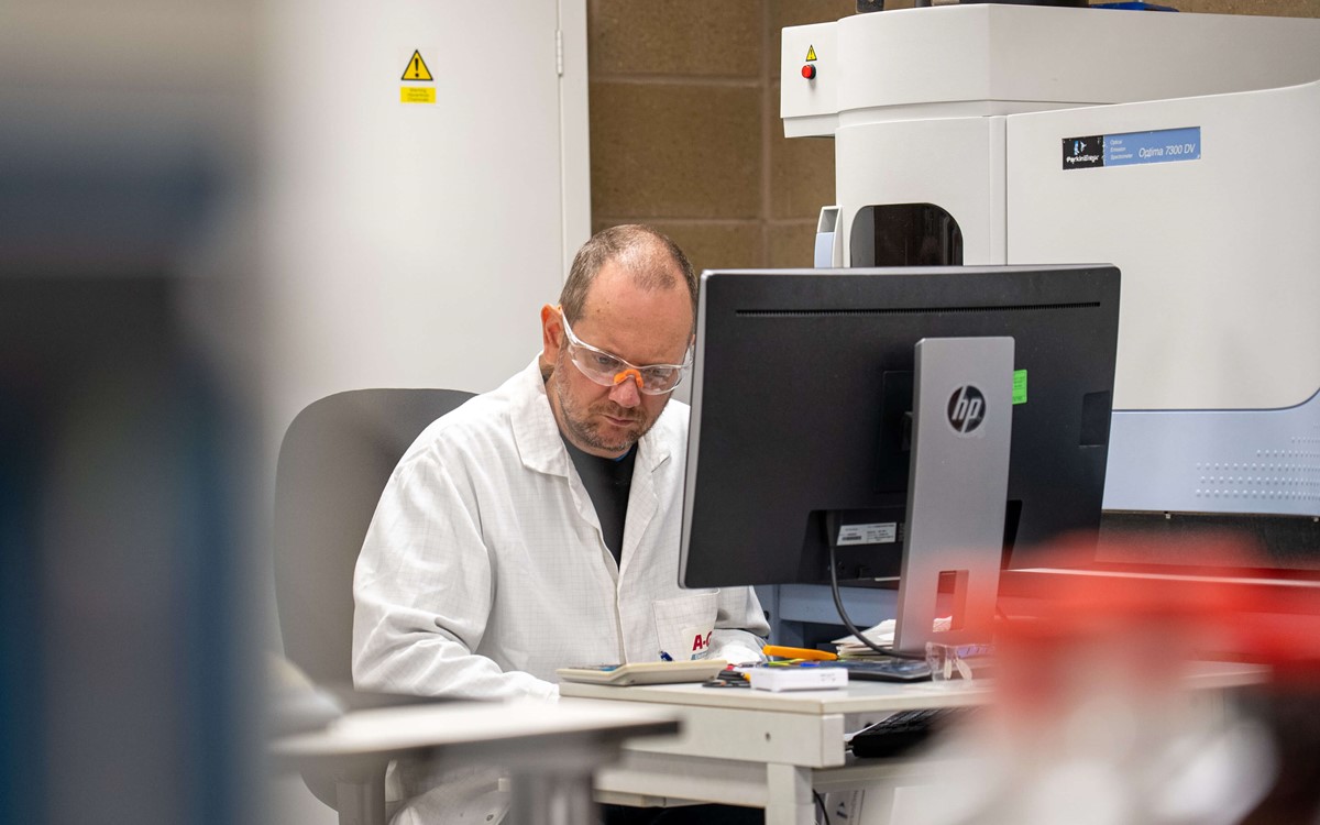 Man in white coat sits at a computer in in laboratory
