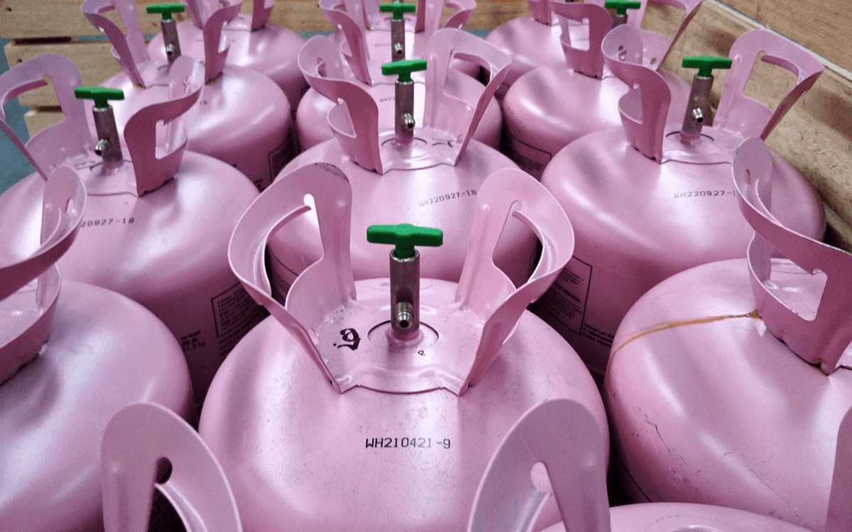Rows of pink disposable cylinders with green valves in a wooden crate