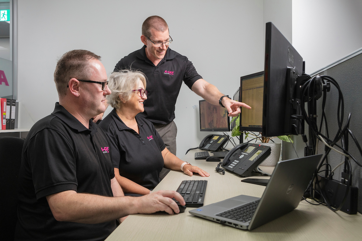 Man pointing at computer screen while smiling next to colleagues in an office