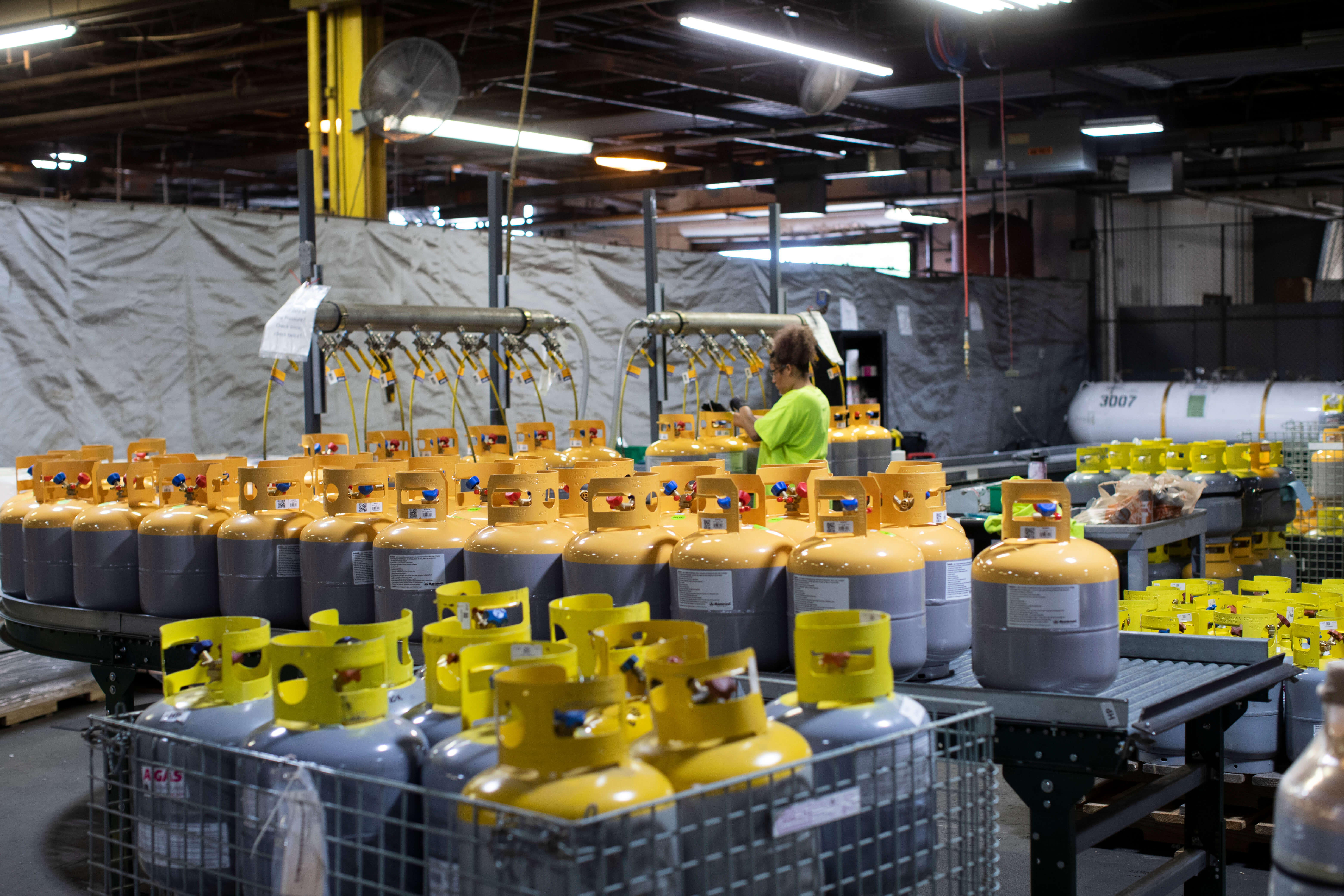 A wide shot of lots of yellow and grey cylinders with a woman working in the warehouse with the cylinders