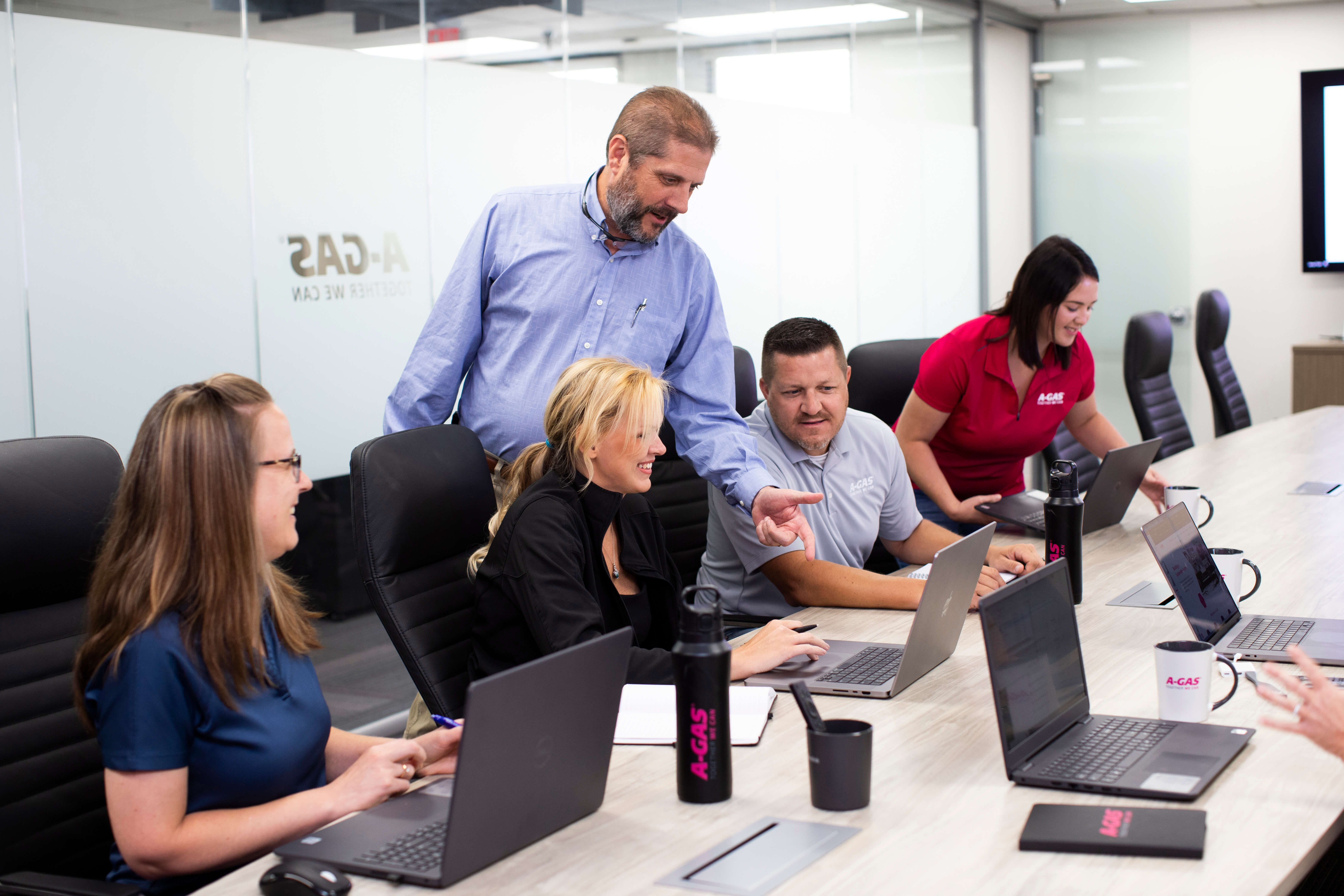 Men and women sat in the boardroom looking at a laptop, there is one man standing up pointing at the screen
