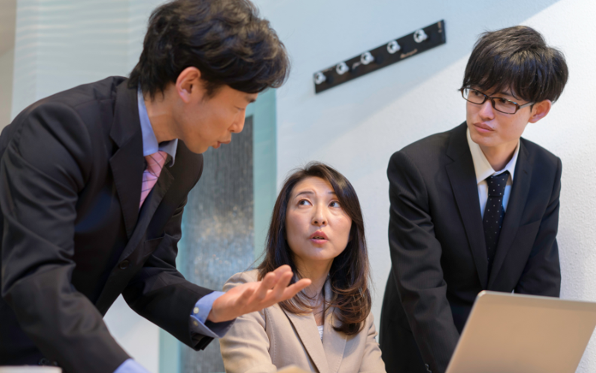 Three formally dressed people talking around a laptop