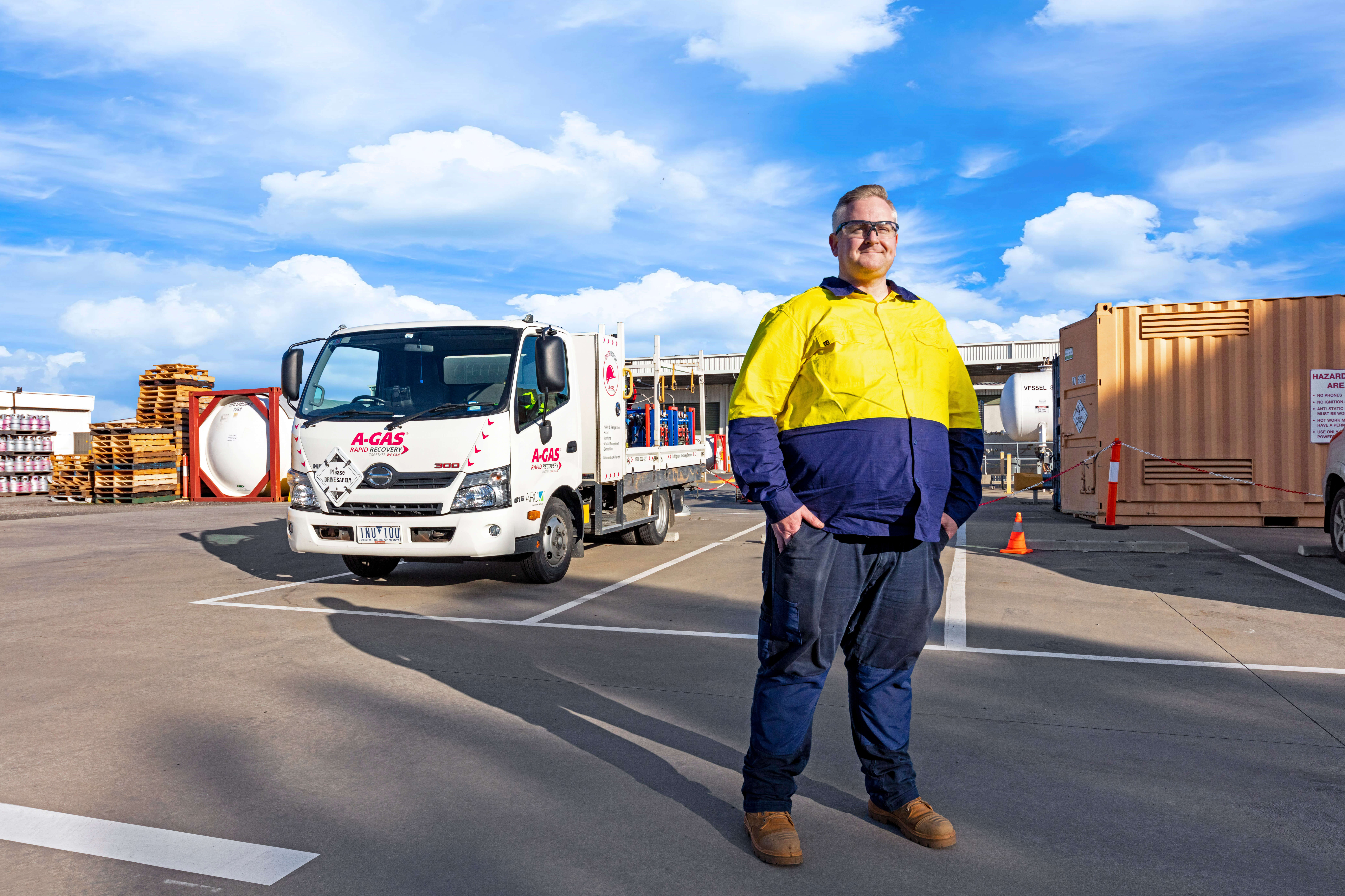 Man standing with hands in pockets in front of white truck and smiling at the camera 