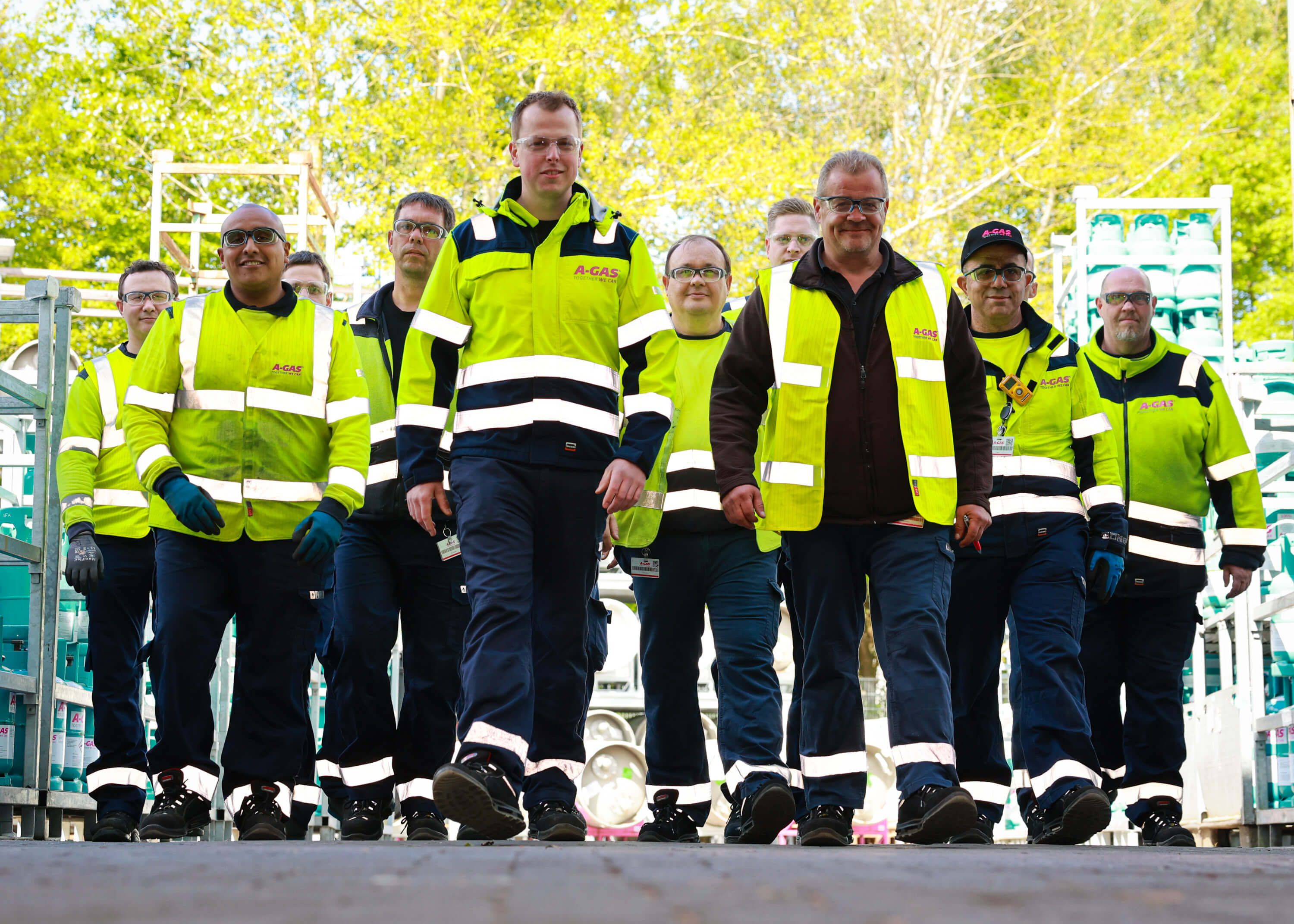 A group of men in yellow high-vis jackets walk towards the camera smiling 
