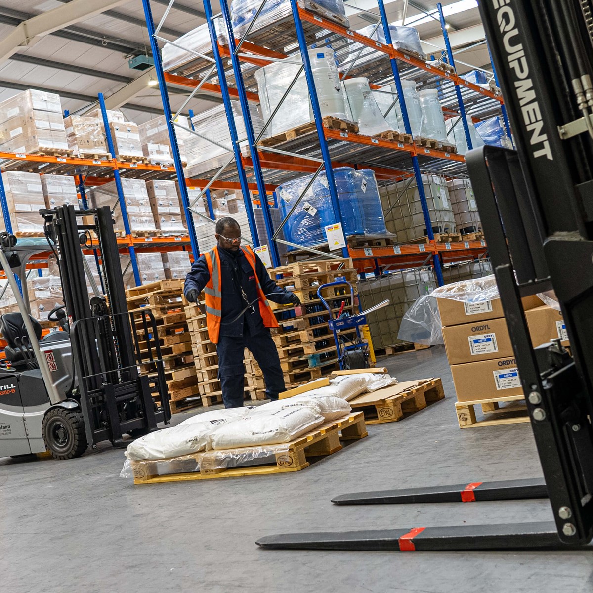 A man piles sacks on pallets between two forklift trucks in warehouse