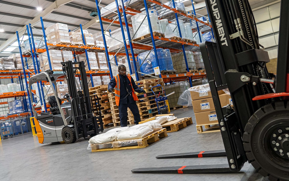 A man piles sacks on pallets between two forklift trucks in warehouse