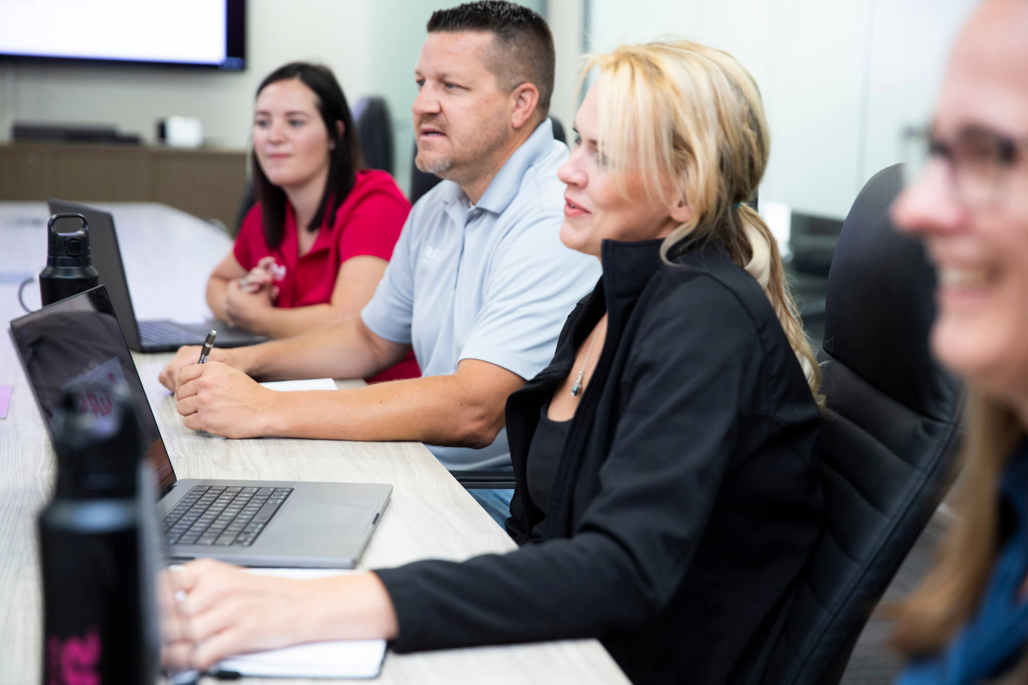 A group of men and women sat around a board room table, they are laughing