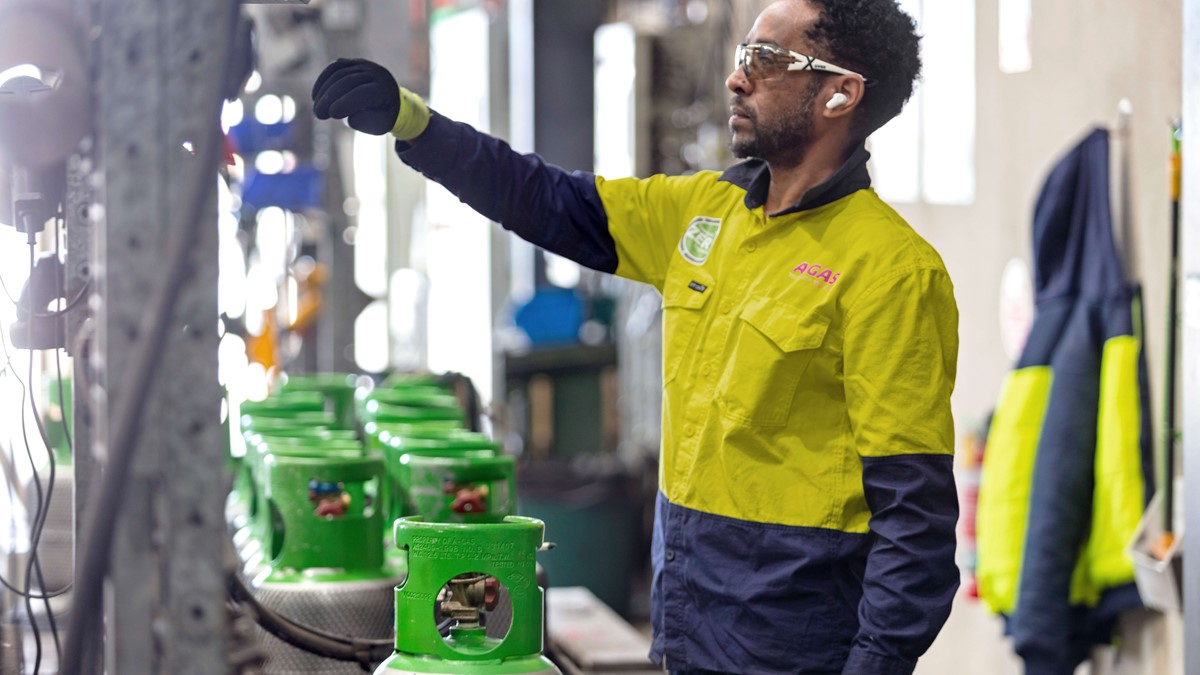 Technician in a yellow and blue high-vis jacket filling a green-topped gas cylinder