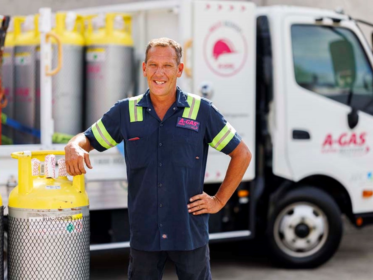 Man leaning against a cylinder in front of a white truck while smiling at the camera