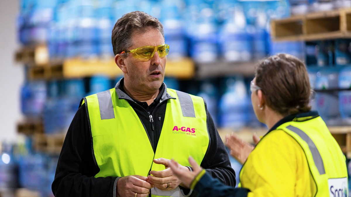 A man and a woman wearing yellow high-vis jackets talking in a warehouse