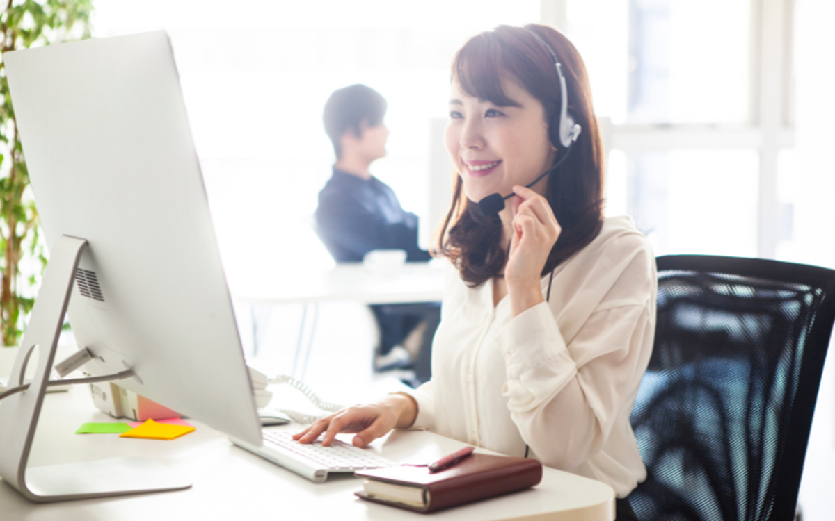 A woman in an office talking into a microphone at a computer